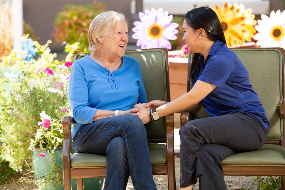 Woman resident and a staff member sitting in the garden talking an holding hands.