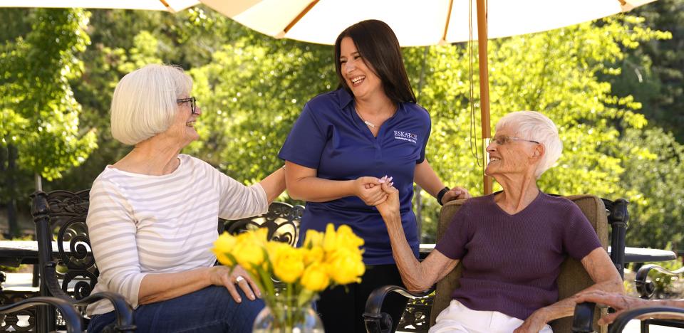 Two women sitting at the patio smiling and talking with a staff member