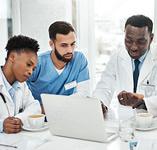 Three doctors sitting at a table looking at a laptop computer 