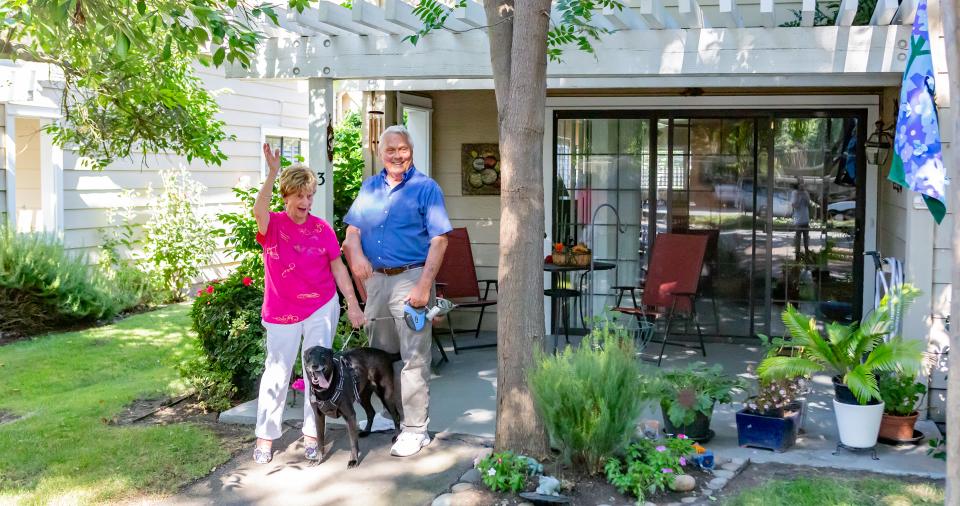 A couple and their dog in front of the cottage waving to friends.