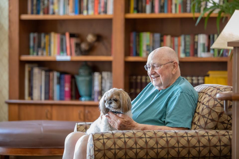 A smiling man sitting in the community library with his dog on his lap.