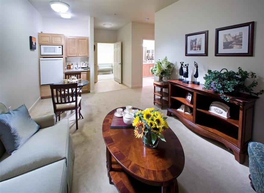 Assisted living apartment living room with couch and chairs, coffee table and bookshelf. 