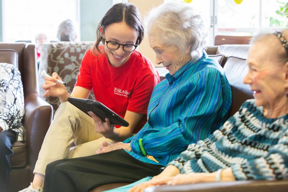 A woman staff member training two resident women how to use an iPad.