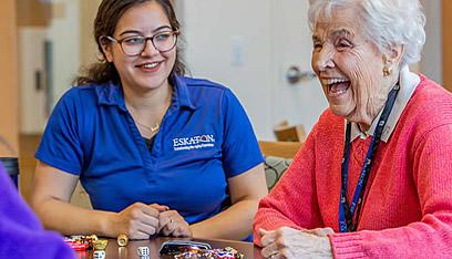 Resident and staff laughing and playing a dice game.